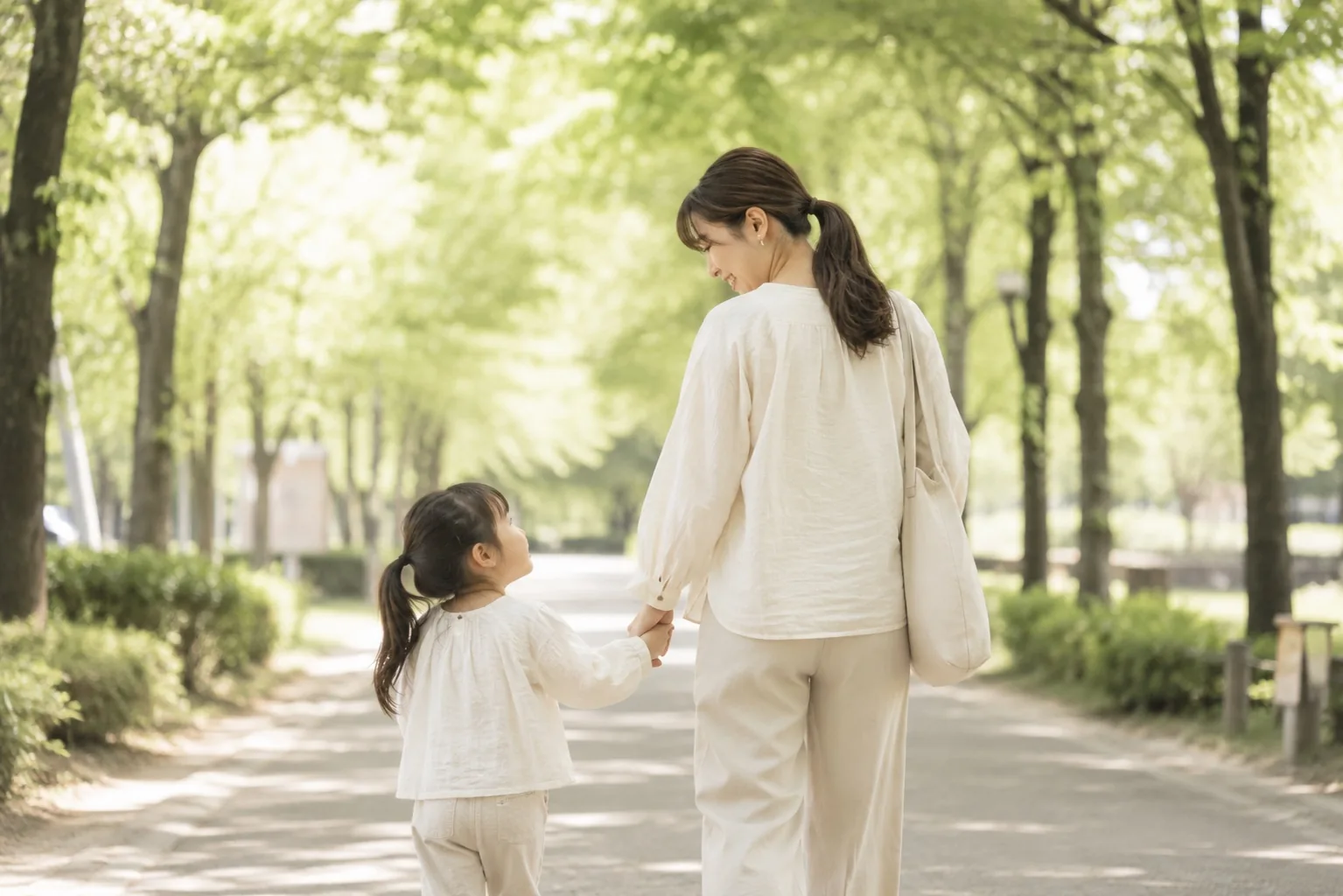 新緑の並木道で手をつないで歩くお母さんと上のお子さま