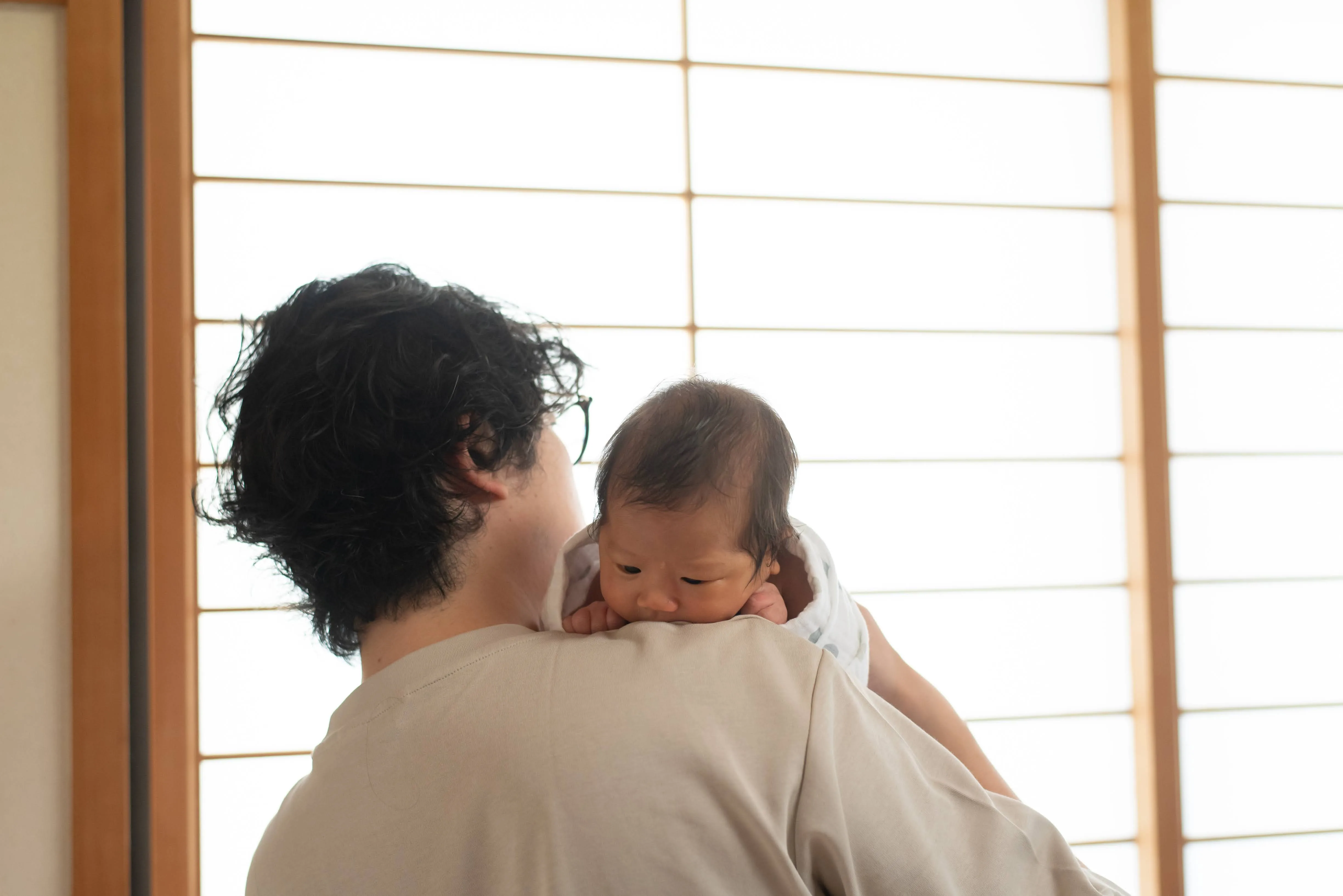 障子の柔らかな光の中、赤ちゃんを抱く父親